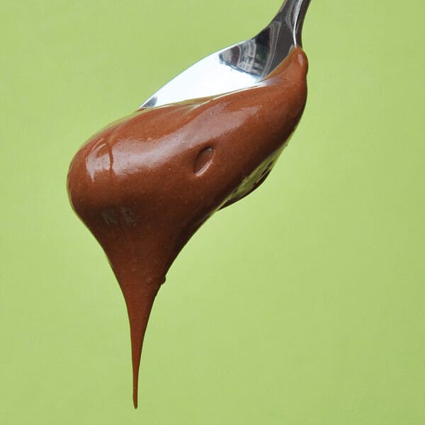 Haselnuss Schoko-Aufstrich fliesst von einem kleinen Löffel vor grünem Hintergrund