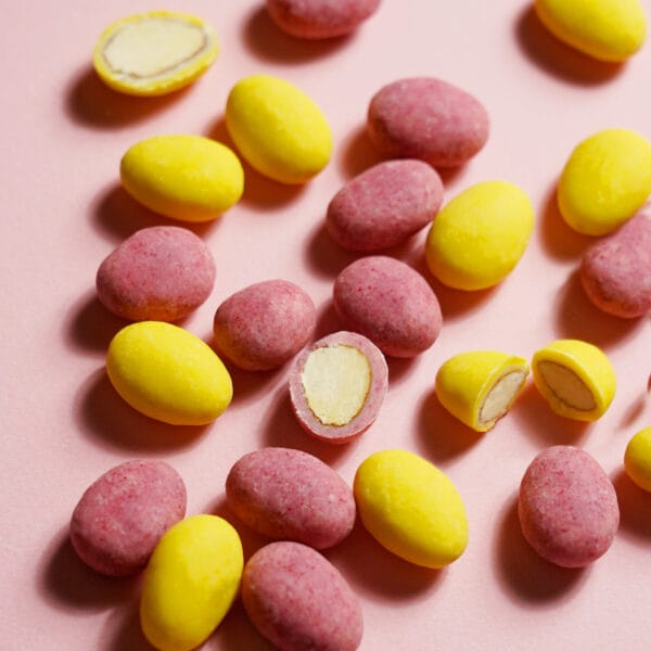 Himbeer-Zitronen-Mandeln-Mix in Gelb und Rosa: Einige schokolierte Mandeln sind aufgeschnitten, sodass die Nuss und die Umhüllung aus Schokolade sichtbar sind