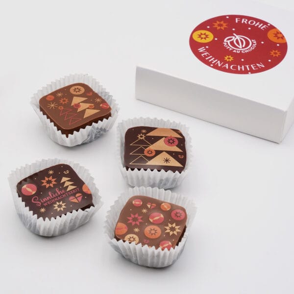 Vier Pralinen mit unterschiedlichen Weihnachts-Illustrationen. Daneben eine weiße Schachtel mit rundem Sticker mit der Aufschrift 'Frohe Weihnachten' und dem Pott au Chocolat Logo. Der Sticker hat einen roten Hintergrund mit Illustrationen von gelben und orangenen Sternen