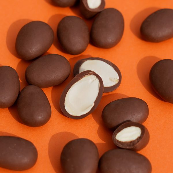 Viele schokolierte Mandeln liegen auf einem orangefarbenen Hintergrund. Einige Mandeln sind aufgeschnitten.