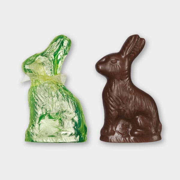Osterhasen-Tafel aus Milchschokolade ausgepackt, daneben eine weitere in grünem Papier eingepackte Tafel mit einer grünen Schleife um den Hals