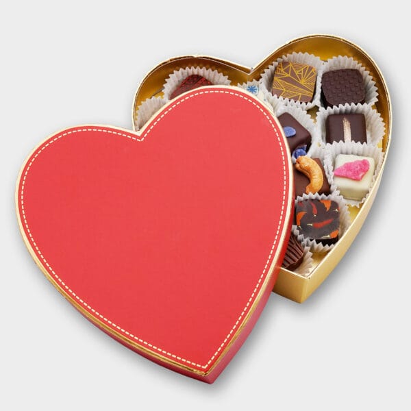 Pralinen in einer goldenen Box mit rotem Deckel in Herzform die halb geöffnet ist