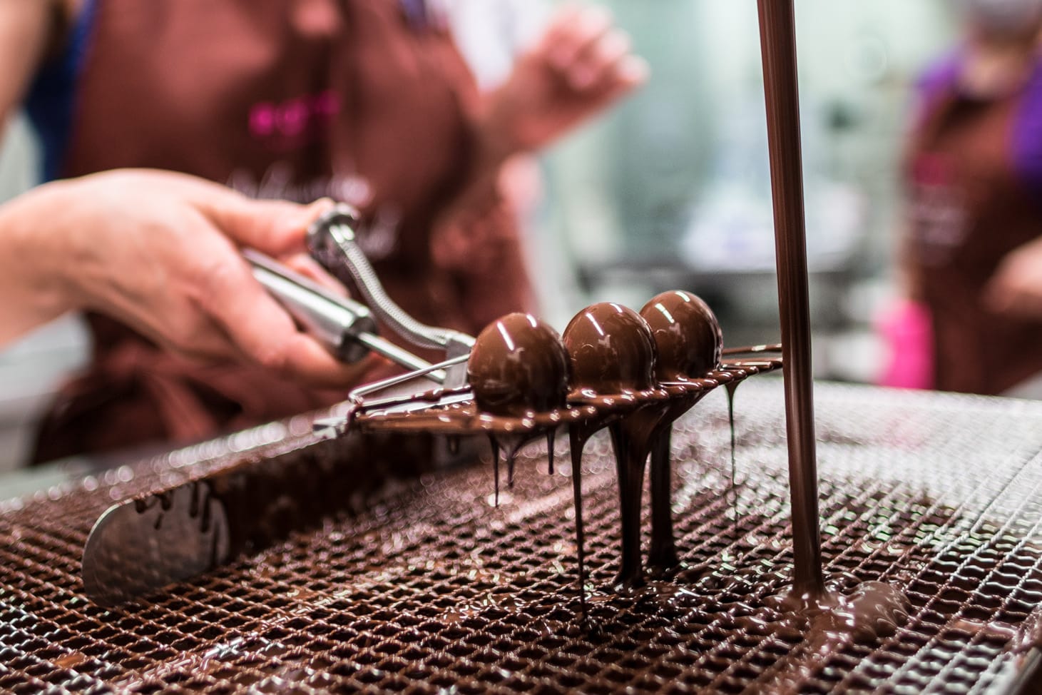 Teilnehmer eines unserer Pralinenseminare beim tauchen von Hohlkörperpralinen in unserer Temperiermaschine