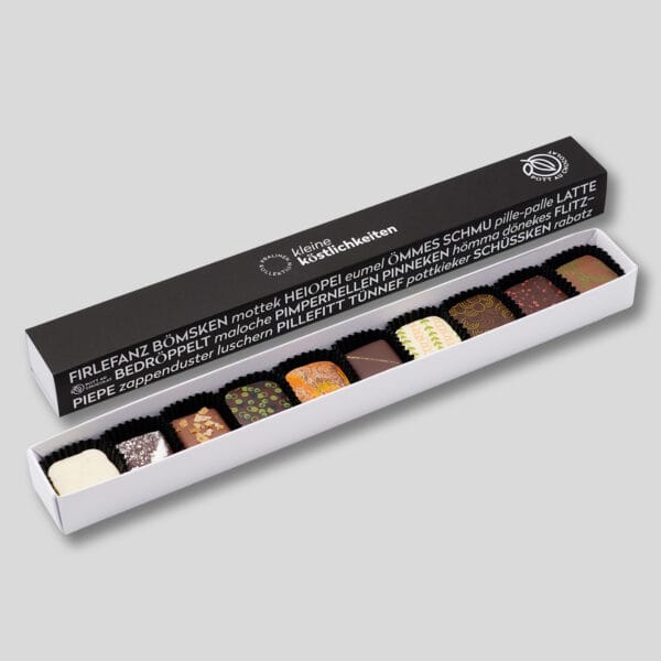 Pralinenstange mit 10 bunt dekorierten Pralinen. Die Banderole ist schwarz mit weißer Schrift. Darauf steht 'Kleine Köstlichkeiten' und verschiedene Wörter, die typisch für das Ruhrgebiet sind. Firlefanz, Bömsken, hömma...