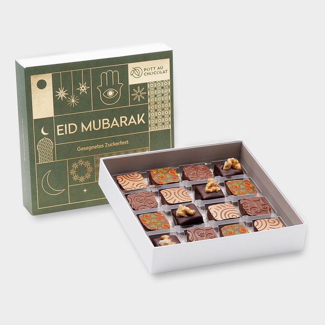 Pralinenschachtel Eid Mubarak. Banderole in grün mit goldener Prägung. Davor steht eine geöffnete Pralinenschachtel mit 16 bunt dekorierten Pralinen