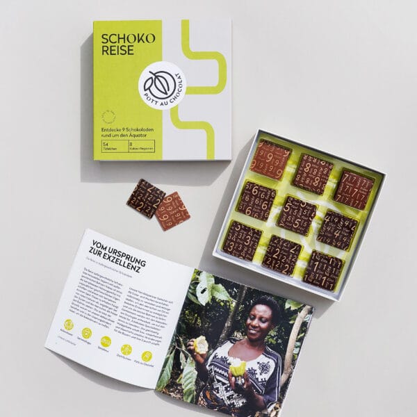 Schoko-Reise' Box mit 9 verschiedenen Probiertafeln. Davor die offene Box mit den Täfelchen und eine aufgeklappte Broschüre mit interessanten Informationen zu den Tafeln