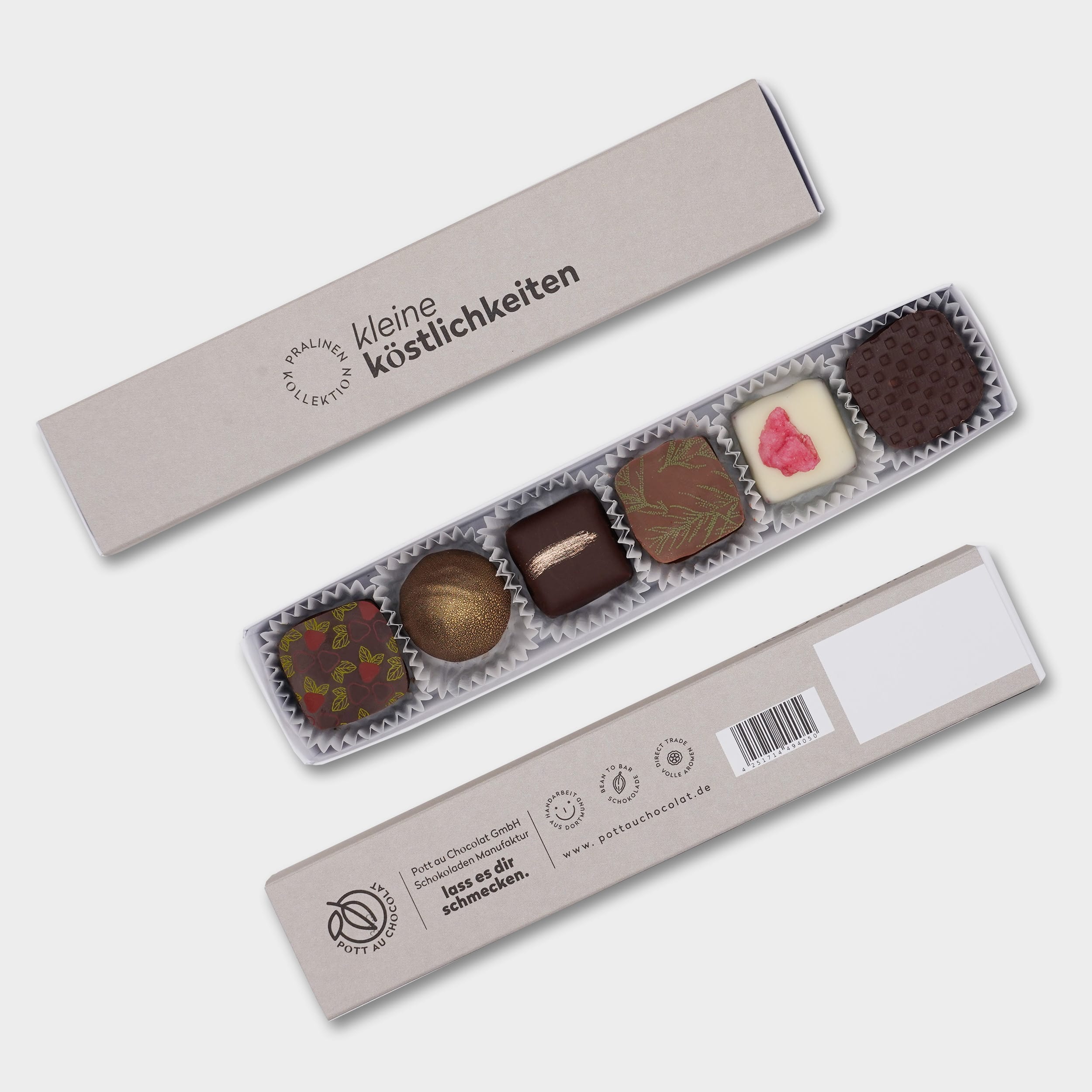 Pralinenstange mit der schwarzen Aufschrift 'Kleine Köstlichkeiten' auf grauem Hintergrund. Davor liegt die Stange geöffnet mit 6 verschiedenen, bunt dekorierten Pralinen. Darunter die Rückseite der Verpackung mit Informationen zu Pott au Chocolat, Logo, EAN Code, Website und 'lass es dir schmecken`.