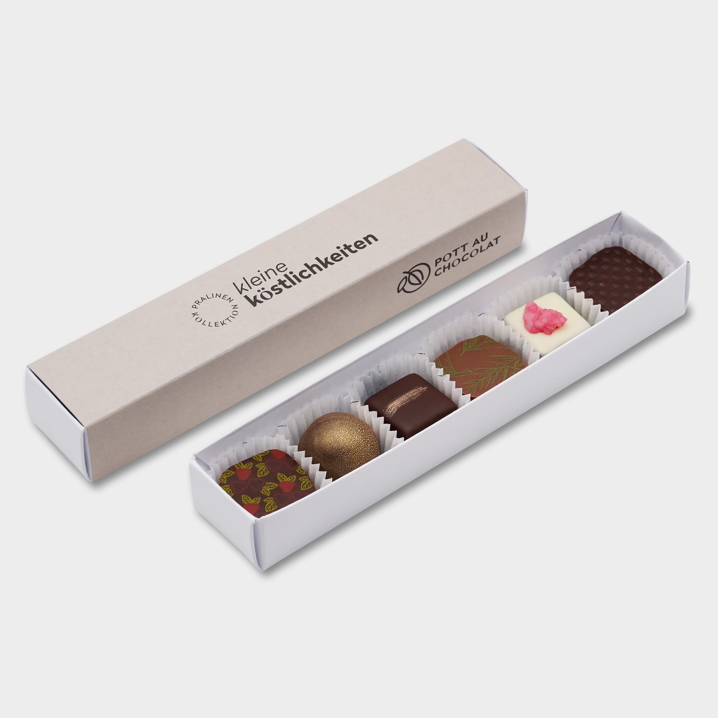 Pralinenstange mit der schwarzen Aufschrift 'Kleine Köstlichkeiten' auf grauem Hintergrund. Davor liegt die Stange geöffnet mit 6 verschiedenen, bunt dekorierten Pralinen.