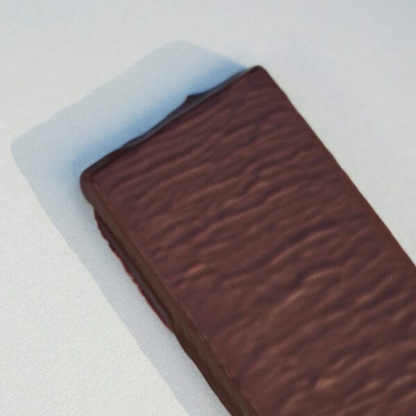 Nahaufnahme von schräg oben auf einen Teil einer mit dunkler Schokolade überzogenen gefüllten Tafel auf einer grauen Fläche