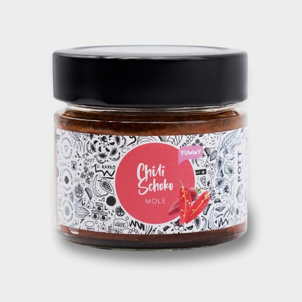 Frontalaufnahme des Einmachglases mit Mole - Chili Schoko Sauce. zu sehen ist das Glas mit Etikett in weiss mit schwarzen Zeichnungen zum Thema Kochen. In der Mitte mit einem roten Kreis mit der Aufschrift und roten Chilisorten. Abgeschlossen mit einem breiten schwarzen Deckel.