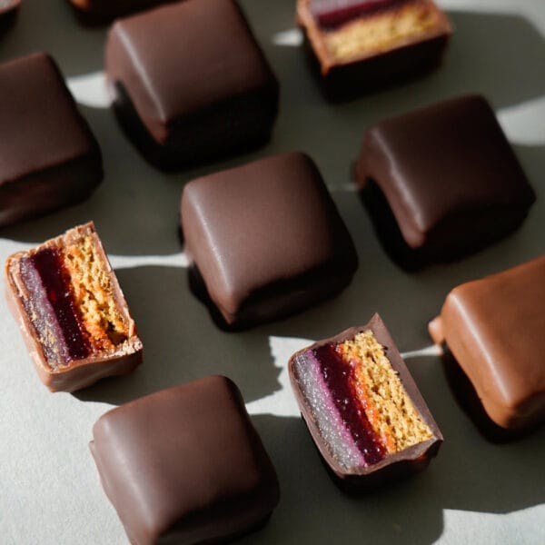 Anordnung von Dominosteinen von oben fotografiert teilweise überzogen mit dunkler oder Milchschokolade einige mittig angeschnitten zeigen den Schichtaufbau des Innenlebens - Honigkuchenteil, Fruchtgelee Himbeere-Johannisbeere, Marzipan und alles umhüllt von Schokolade