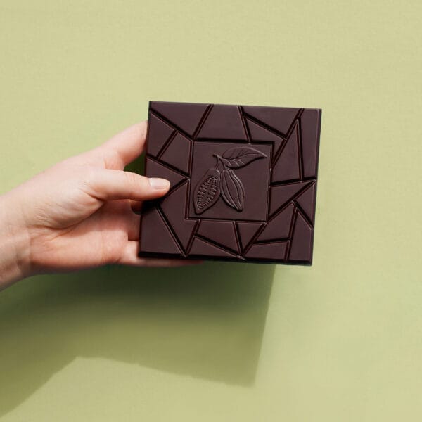 Dunkle Schokoladentafel wird von einer Hand vor einer grünen Wand gehalten