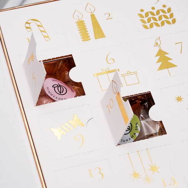 Zwei Türchen des Adventskalenders sind geöffnet. Darin jeweils ein Tütchen mit Sticker und schokladigen Produkten darin.