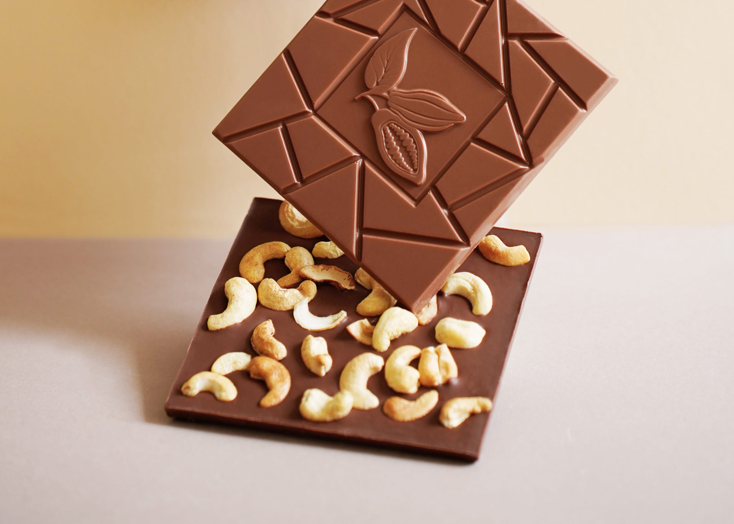 Zwei Milch-Schokoladen Tafeln übereinander. Eine ist belegt mit Cashew Kernen.