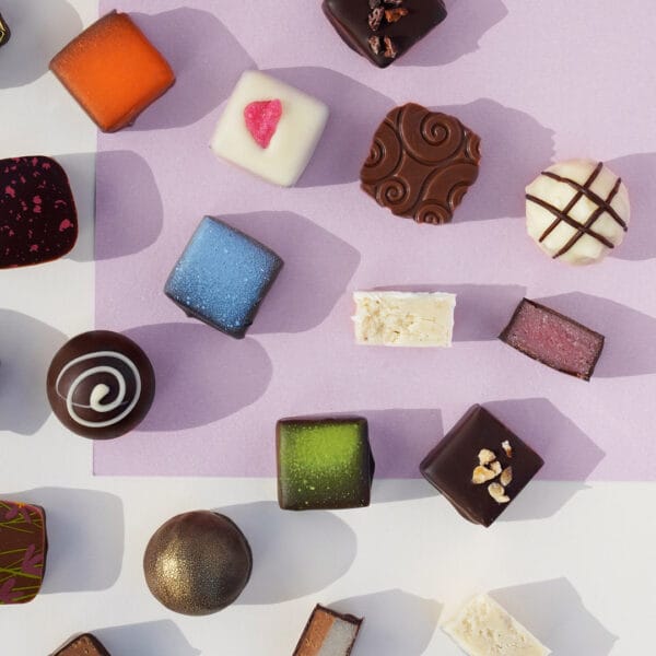 Verschiedene Sorten Pralinen von Pott au Chocolat angeordnet auf farbigem Untergrund, einige davon angeschnitten