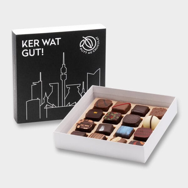 Aufgestellte schwarze Pralinenbox mit der Aufschrift 'Ker Wat Gut' und der Dortmunder Skyline in Weiß. Davor steht die offene Pralinenbox mit verschiedenen Sorten Pralinen