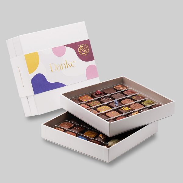 Pott au Chocolat weisse Pralinenbox mit 50 Pralinen und einer bunten Banderole aus Farbmustern in Blau, Grau, Gelb braun und Rosa mittig die Gold geprägte Aufschrift "Danke"