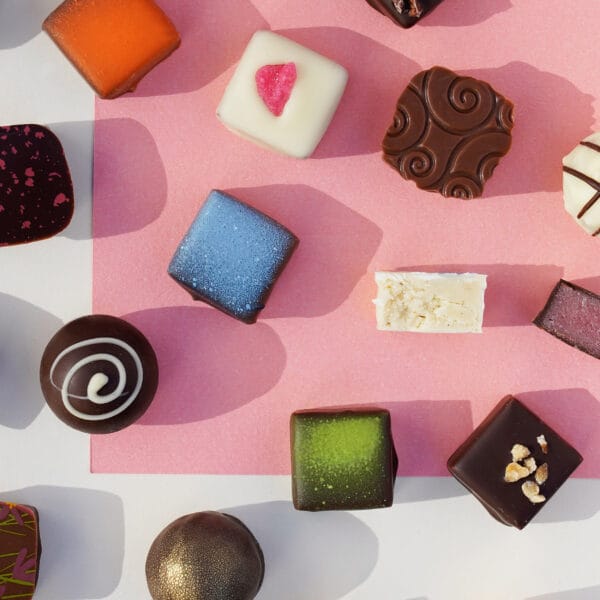 Verschiedene Sorten Pralinen von Pott au Chocolat angeordnet auf farbigem Untergrund, einige davon angeschnitten