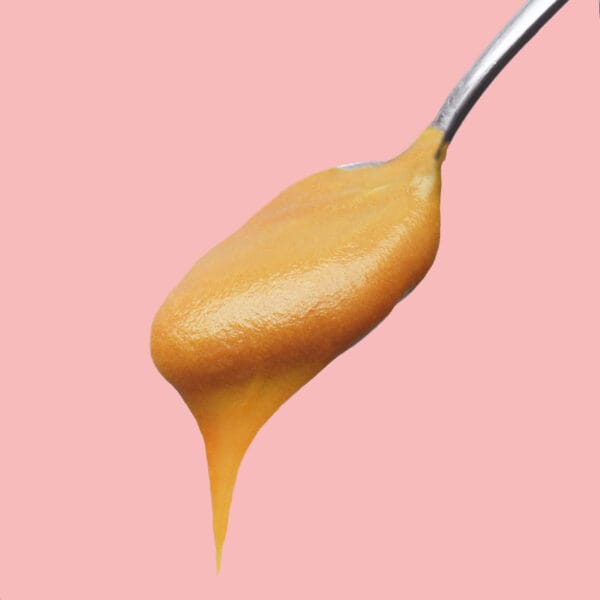 Karamel-Aufstrich fliesst von einem kleinen Löffel vor pinkem Hintergrund